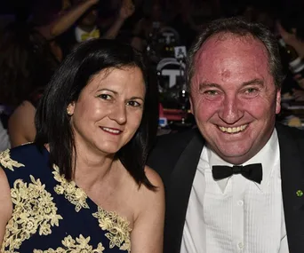 A smiling couple dressed formally, attending an event, with other attendees blurred in the background.