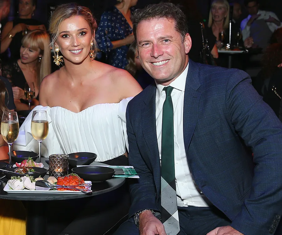 A couple smiles at a table with drinks and appetizers at a fashion event.