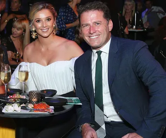 A couple smiles at a table with drinks and appetizers at a fashion event.