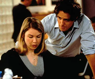 Two office workers in discussion; a woman seated, a man leaning over with a serious expression.