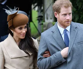 A couple walking arm in arm, the woman in a brown hat and coat, the man in a grey suit with a tie.