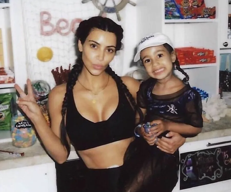Woman in a black top and braided hair poses with a child in a store. The woman flashes a peace sign.