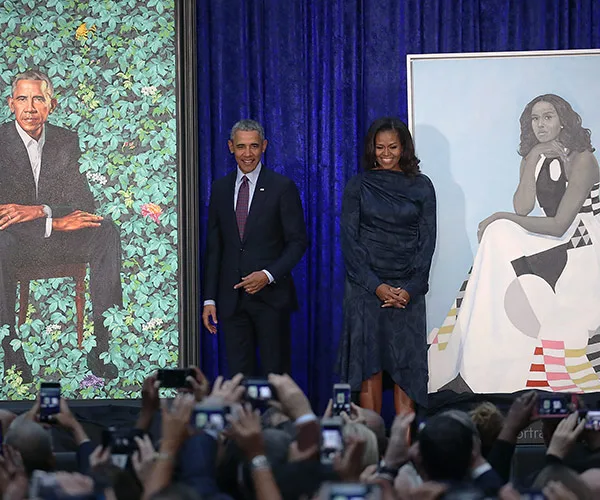 Barack and Michelle Obama unveil their official portraits in a gallery setting, with people capturing the moment on phones.