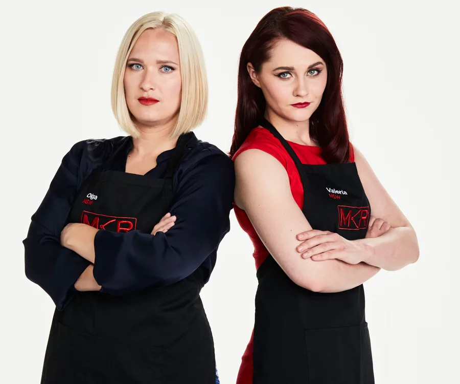 Two women from "My Kitchen Rules," Olga and Valeria, posing with arms crossed, wearing black aprons.