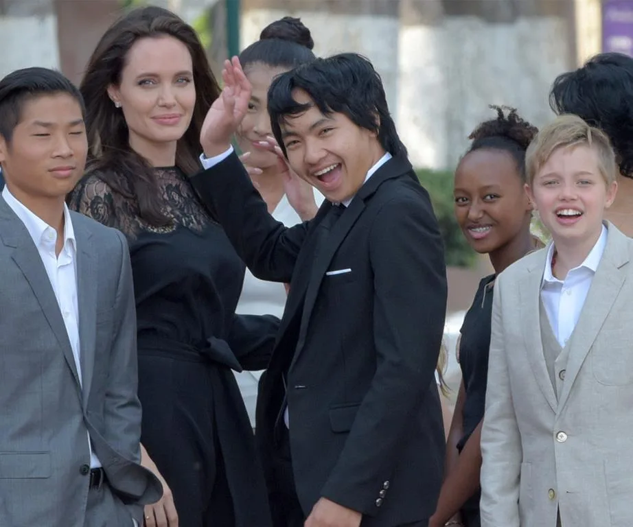 A group photo with Angelina Jolie and several children in formal attire, smiling at an outdoor event.