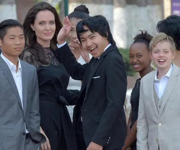 A group photo with Angelina Jolie and several children in formal attire, smiling at an outdoor event.