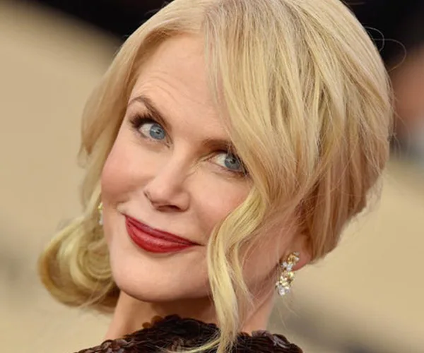 Actress with blonde hair and red lipstick at an event, smiling at the camera.