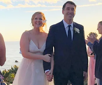 Bride and groom smiling, holding hands at sunset wedding by the ocean.