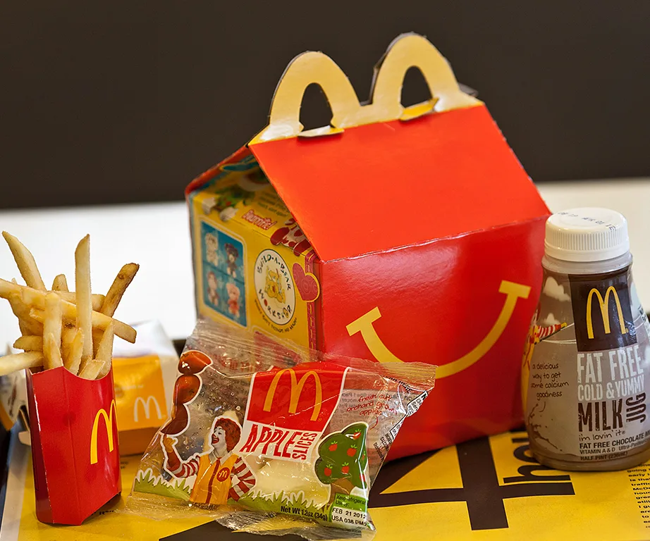 McDonald's Happy Meal with fries, apple slices, chocolate milk, and a red box featuring a smiley face logo.