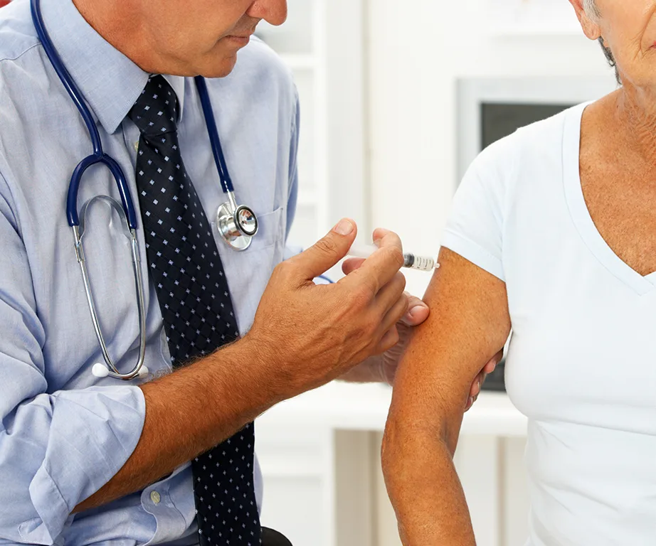 Doctor administering flu vaccine to older patient in clinic.