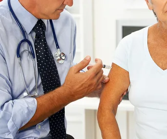 Doctor administering flu vaccine to older patient in clinic.