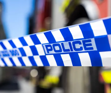 Police tape with blurred background, indicating crime scene area.