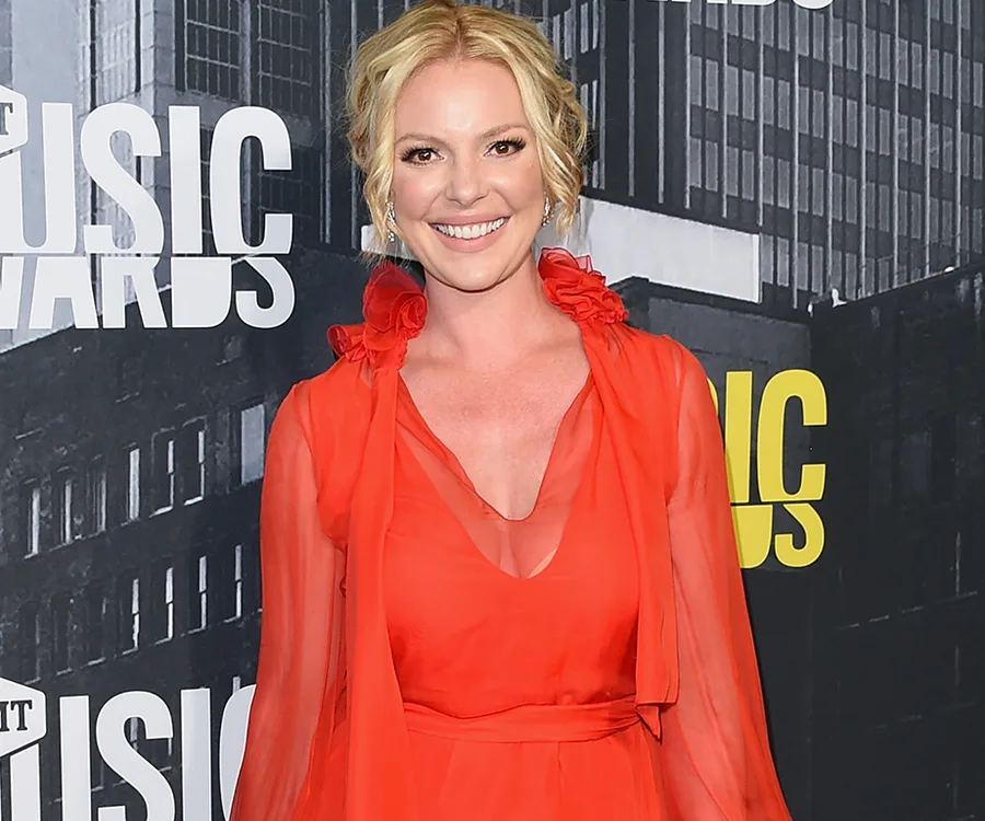 A woman in a red dress smiling at an awards event, with a city backdrop.