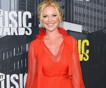 A woman in a red dress smiling at an awards event, with a city backdrop.