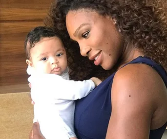 A woman with curly hair holds a baby, both looking content and close.