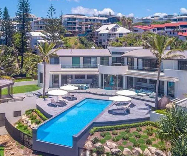 Luxurious Queensland home with a pool and modern architecture set against a backdrop of lush greenery and neighboring houses.