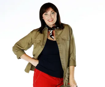 A person smiling, wearing a khaki shirt, black top, red pants, and a scarf, against a plain white background.