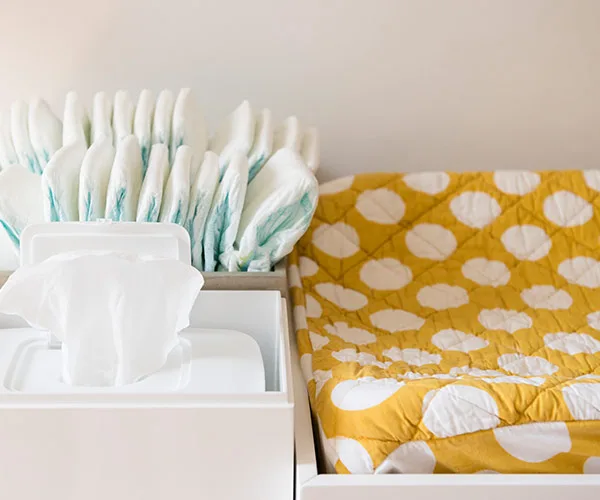 Diaper changing station with wipes and stacked diapers next to a yellow polka dot-patterned changing mat.