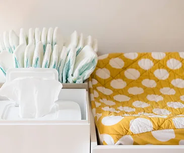 Diaper changing station with wipes and stacked diapers next to a yellow polka dot-patterned changing mat.