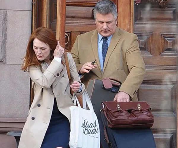 Man and woman in coats carrying bags and briefcase, standing near a door.