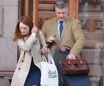 Man and woman in coats carrying bags and briefcase, standing near a door.