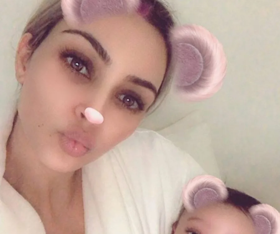 Woman with animal-ear filter takes a selfie, holding a baby with matching filter.