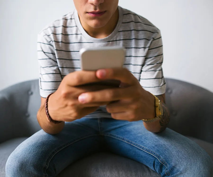 Teenager in striped shirt sitting on a couch, intently using a smartphone, highlighting focus on digital communication.
