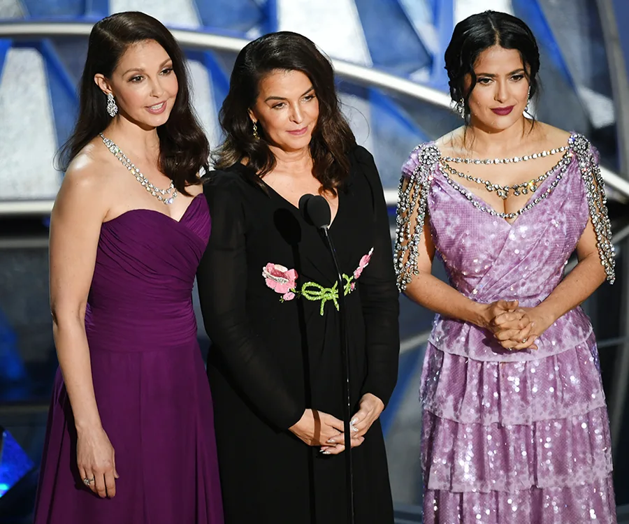 Three women stand together on stage at the 2018 Oscars, dressed elegantly in evening gowns.
