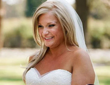 Bride smiling in wedding dress with long blonde hair and veil, outdoors.
