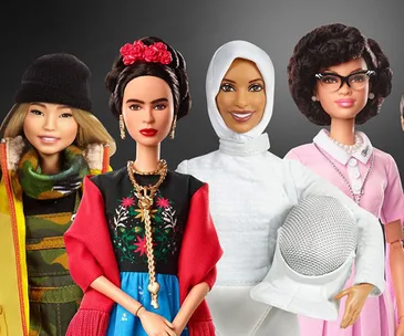 Barbie dolls representing diverse and influential women, including a skier, artist, fencer, and a historical figure, posed together.