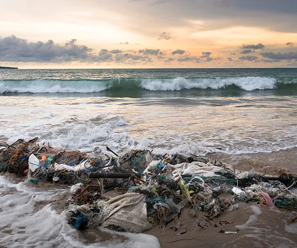 Ocean waves against a Bali beach with plastic debris washed ashore at sunset.