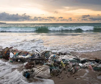 Ocean waves against a Bali beach with plastic debris washed ashore at sunset.