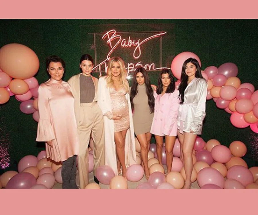 Group of women posing at a baby shower with pink and peach balloons in the background.