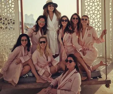 Group of women in matching robes and sunglasses, smiling and posing in a sunny outdoor setting.