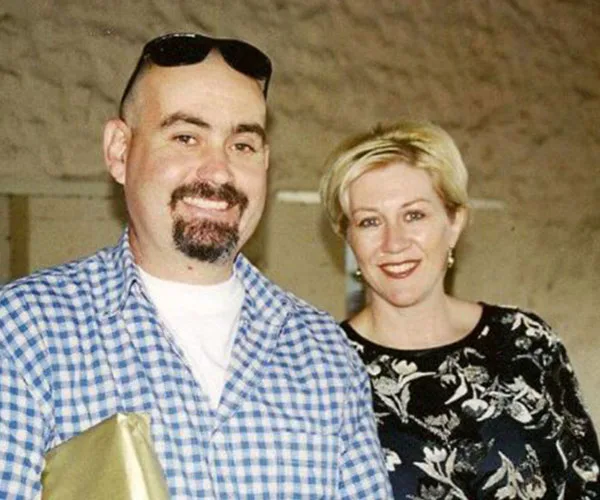 Man and woman smiling together, man in checkered shirt holding a golden package, indoors.