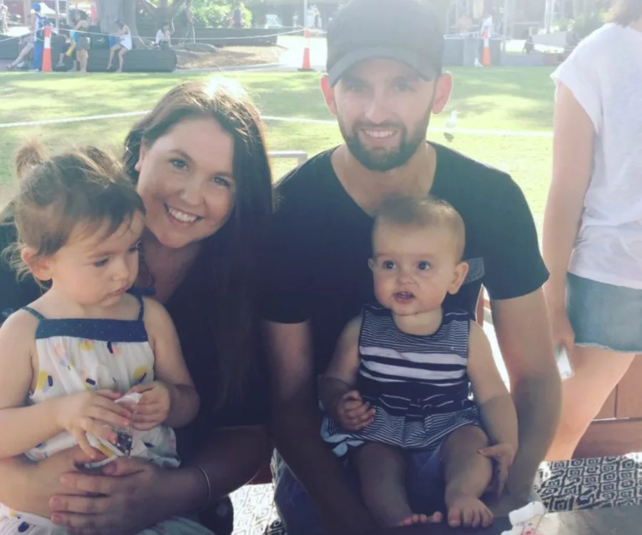 A family of four sitting outdoors, with a man, woman, and two children enjoying a sunny day.