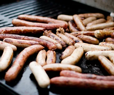 Grilled sausages of various types and sizes cooking on a barbecue grill.