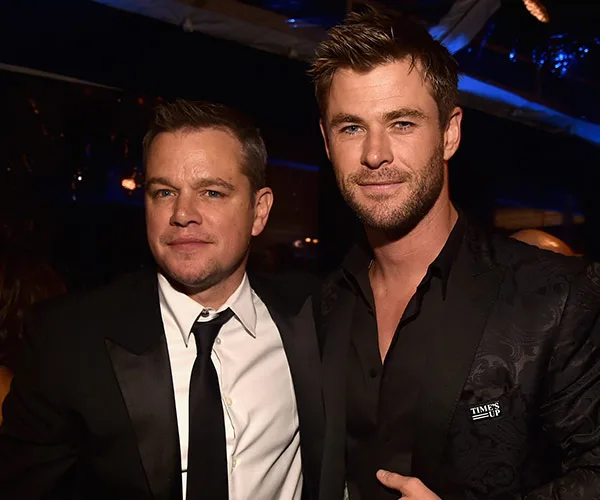 Two men in suits pose for a photo at an event, smiling under dim, warm lighting.