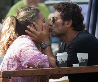 A couple kissing at an outdoor cafe with coffee cups labeled "Love Masters" on the table.