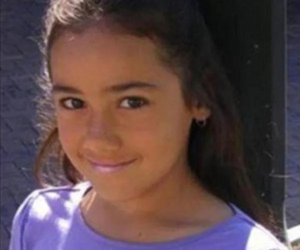 A young girl with long hair, wearing a purple shirt, smiling at the camera.