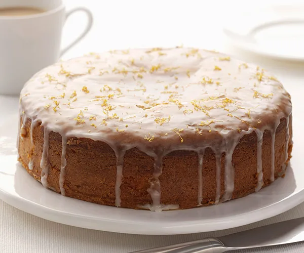 Lemon and elderflower cake with white icing and lemon zest on top, served on a white plate.