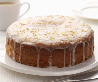 Lemon and elderflower cake with white icing and lemon zest on top, served on a white plate.