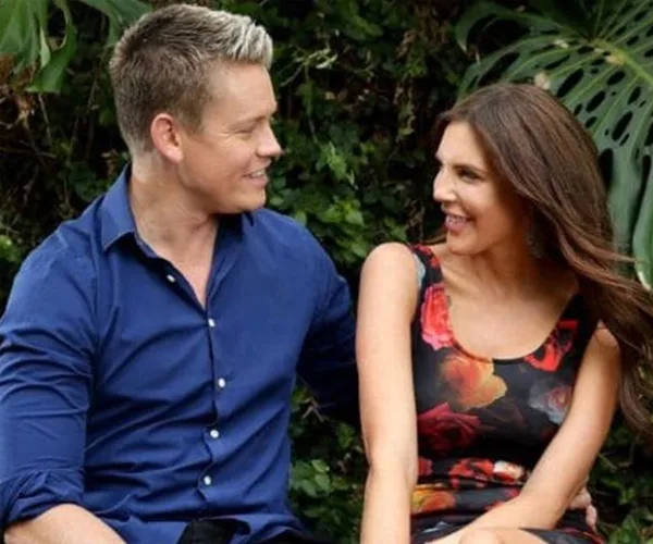 A couple seated outdoors, smiling and looking at each other affectionately.