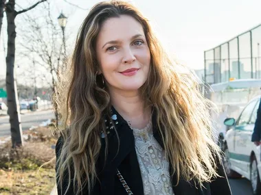 A person with long wavy hair and a lace top smiles outdoors on a sunny day.