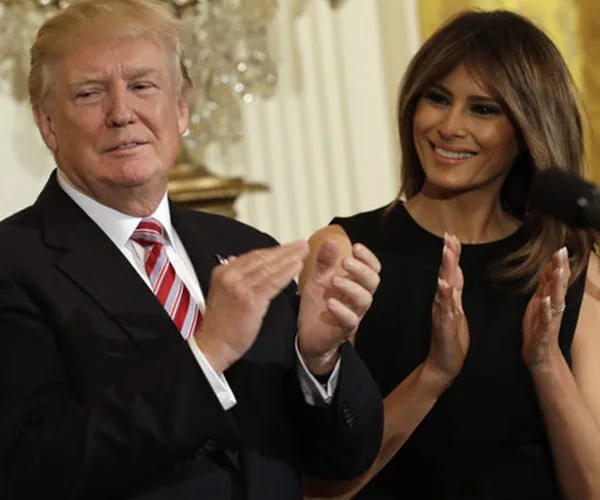 Donald and Melania Trump clapping together at an event, both smiling.