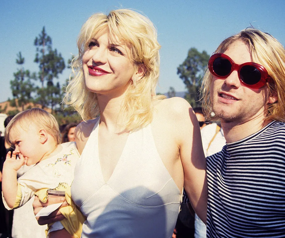 A smiling couple with a toddler, outdoors, sunny day.