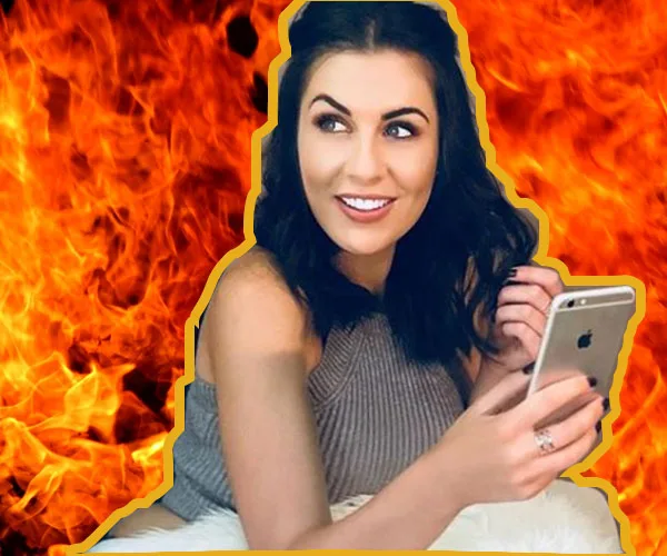Young woman with dark hair holding a smartphone, smiling, with a fiery background.