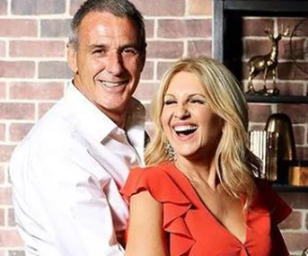 Man and woman smiling in front of a brick wall, the woman in an orange dress and the man in a white shirt.