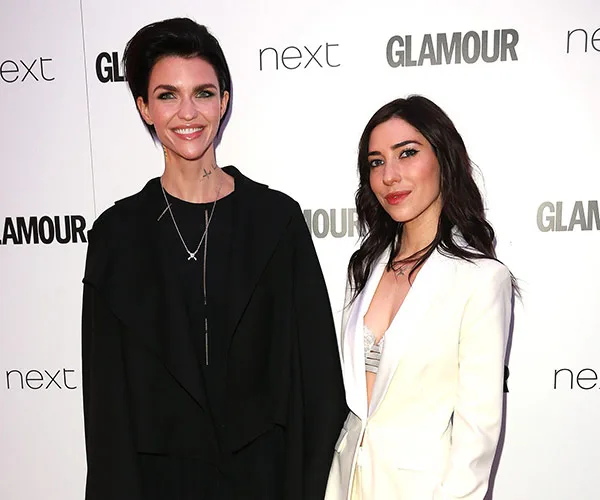 Two individuals pose together at a Glamour event; one in black attire, the other in a white suit.
