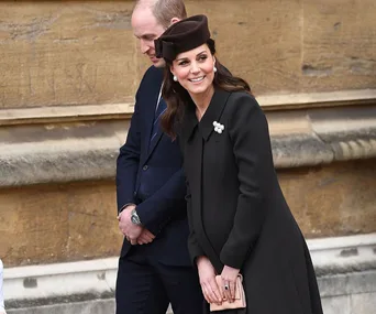 Duchess Kate at Easter service in a dark coat and hat, smiling beside another individual.